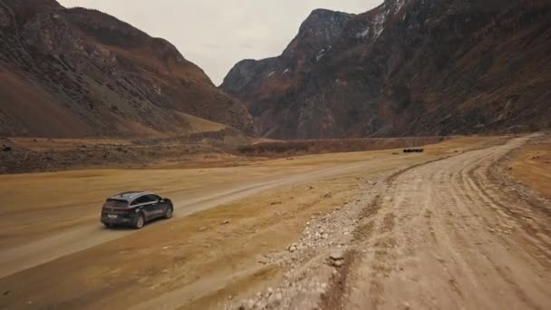 A black SUV jeep car is driving along an empty country road in the huge Katu-Yaryk canyon Chulyshman Valley with a large mountain bubbling river. Altai, Siberia, Russia. People travel along a dirt — Stock Video