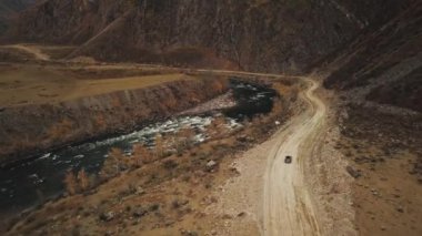 Büyük bir dağ köpüren nehri olan Katu-Yaryk kanyonu Chulyshman Vadisi 'nde boş bir köy yolunda siyah bir SUV aracı sürüyor. Altai, Sibirya, Rusya. İnsanlar kir içinde seyahat eder.