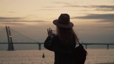 Bir kız ZSD köprüsünün arka planında gün batımını fotoğraflıyor. Akşam Stereoleto Yaz Müzik Festivali 'nde genel atmosfer, Saint Petersburg, Sevkabel 2020. İnsanları geçiyor.
