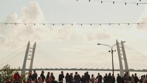 Mensen, bezoekers zitten aan het water van de Finse Golf op de achtergrond van de ZSD brug. De algemene sfeer op het Stereoleto Summer Music Festival, Sint-Petersburg, Sevkabel 2020. Mensen — Stockvideo