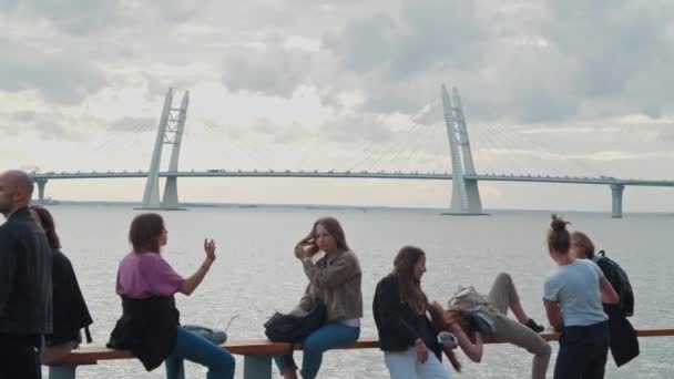 Люди, відвідувачі, сидять біля води Фінської затоки на задньому плані мосту ЗСД. Загальна атмосфера на Літньому музичному фестивалі Stereoleto, Санкт-Петербург, Севкабель 2020. Люди — стокове відео