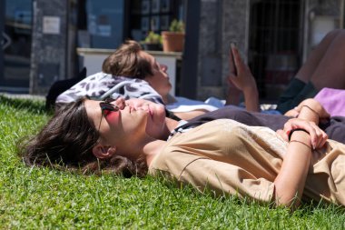 Ligurian Denizi, İtalya - 13 Temmuz 2021: İki yorgun kız plaj diskosunda bir gece geçirdikten sonra halk parkında uyuyor