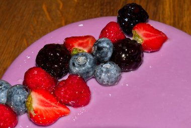 Pembe krema ve taze böğürtlenlerle kaplı bir doğum günü pastasının yakın plan fotoğrafı.