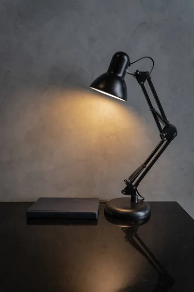 Retro black metal desk lamp or flexible table lamp light bulb on the black table and blue book with cement loft-style wall interior vintage design contemporary. Modern house building concept.
