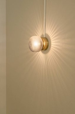 Güzel, modern duvar lambası yuvarlak cam şeklindeki güneş ışınları gibi ışık veriyor ve sarı duvar arka planında yaşıyor. İç aydınlatma ampullerini çağdaş kavramsal olarak inşa et.