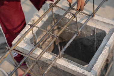 İnşaat işçileri çelik inşaat demirini el telleriyle sağlamlaştırarak inşaat alanı için kiriş çeliğini bağlıyorlar. Metalde çalışan konsept işçiler ve mimarlık için demir takviyesi.