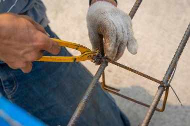 İnşaat işçileri çelik inşaat demirini el telleriyle sağlamlaştırarak inşaat alanı için kiriş çeliğini bağlıyorlar. Metalde çalışan konsept işçiler ve mimarlık için demir takviyesi.