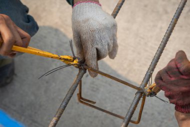 İnşaat işçileri çelik inşaat demirini el telleriyle sağlamlaştırarak inşaat alanı için kiriş çeliğini bağlıyorlar. Metalde çalışan konsept işçiler ve mimarlık için demir takviyesi.