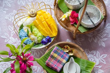 Muz yaprağında hindistan cevizi sütüyle karıştırılmış mangolu pirinç, ahşap masada beyaz seramik tabak ve beyaz giysi örtüsü Tayland 'da yaygın olarak kullanılan geleneksel bir tatlıdır. Meyve tatlısı..