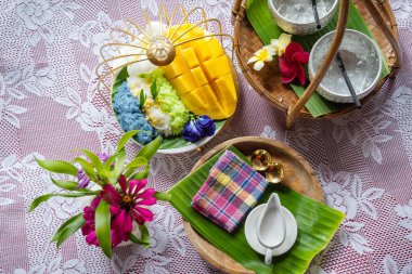 Muz yaprağında hindistan cevizi sütüyle karıştırılmış mangolu pirinç, ahşap masada beyaz seramik tabak ve beyaz giysi örtüsü Tayland 'da yaygın olarak kullanılan geleneksel bir tatlıdır. Meyve tatlısı..