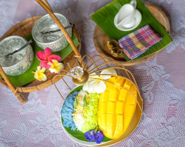 Muz yaprağında hindistan cevizi sütüyle karıştırılmış mangolu pirinç, ahşap masada beyaz seramik tabak ve beyaz giysi örtüsü Tayland 'da yaygın olarak kullanılan geleneksel bir tatlıdır. Meyve tatlısı..