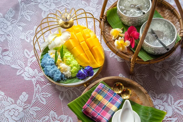 Muz yaprağında hindistan cevizi sütüyle karıştırılmış mangolu pirinç, ahşap masada beyaz seramik tabak ve beyaz giysi örtüsü Tayland 'da yaygın olarak kullanılan geleneksel bir tatlıdır. Meyve tatlısı..