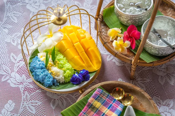 Muz yaprağında hindistan cevizi sütüyle karıştırılmış mangolu pirinç, ahşap masada beyaz seramik tabak ve beyaz giysi örtüsü Tayland 'da yaygın olarak kullanılan geleneksel bir tatlıdır. Meyve tatlısı..