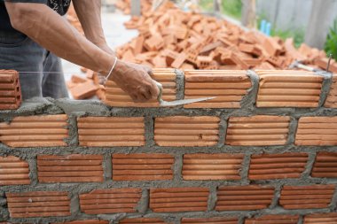 Construction worker installing bricks masonry bricklayer and adjusting bricks walls using trowel, mortar and putty knife. Concept construction work in the countryside building.
