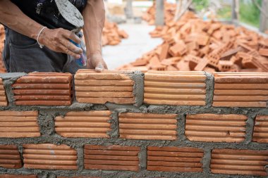 İnşaat işçisi tuğla ustası, tuğla ustası ve tuğla duvarları mala, havan topu ve macun bıçağıyla düzenliyor. Kırsal binalarda konsept inşaat işi.