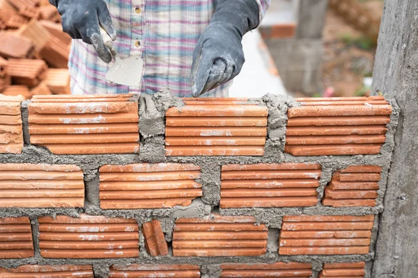 Construction worker installing bricks masonry bricklayer and adjusting bricks walls using trowel, mortar and putty knife. Concept construction work in the countryside building.