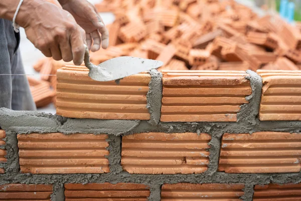 İnşaat işçisi tuğla ustası, tuğla ustası ve tuğla duvarları mala, havan topu ve macun bıçağıyla düzenliyor. Kırsal binalarda konsept inşaat işi.