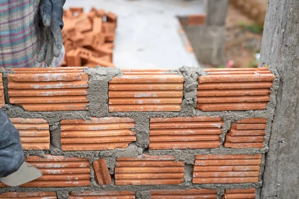 İnşaat işçisi tuğla ustası, tuğla ustası ve tuğla duvarları mala, havan topu ve macun bıçağıyla düzenliyor. Kırsal binalarda konsept inşaat işi.