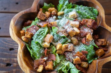 Salamlı Sezar salatası ahşap bir kasede, zeytinyağı, limon suyu, çiğ yumurta, parmesan peyniri ve Sezar soslu baharatlarla servis edilir. Uluslararası lezzetli yiyecekler.