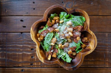 Salamlı Sezar salatası ahşap bir kasede, zeytinyağı, limon suyu, çiğ yumurta, parmesan peyniri ve Sezar soslu baharatlarla servis edilir. Uluslararası lezzetli yiyecekler.