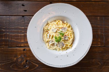 Spagetti Carbonara Makarnası geleneksel İtalyan mutfağının lezzetli yemeğidir. Domuz pastırmalı, maydanozlu, parmesan peynirli ve ahşap masadaki jambonlu ev yapımı krema sosu. Üst görünüm kavramı.