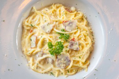 Spagetti Carbonara Makarnası geleneksel İtalyan mutfağının lezzetli yemeğidir. Domuz pastırmalı, maydanozlu, parmesan peynirli ve ahşap masadaki jambonlu ev yapımı krema sosu. Üst görünüm kavramı.