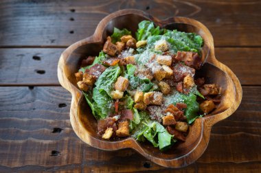 Salamlı Sezar salatası ahşap bir kasede, zeytinyağı, limon suyu, çiğ yumurta, parmesan peyniri ve Sezar soslu baharatlarla servis edilir. Uluslararası lezzetli yiyecekler.