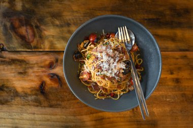 Kızarmış Spagetti Makarnası, çıtır çıtır domuz pastırması, lezzetli yemekler ve güzel ahşap bir masadaki gri seramik tabakta servis edilen kurutulmuş biber. Pek çok insan için sağlıklı favori yemek kavramı.