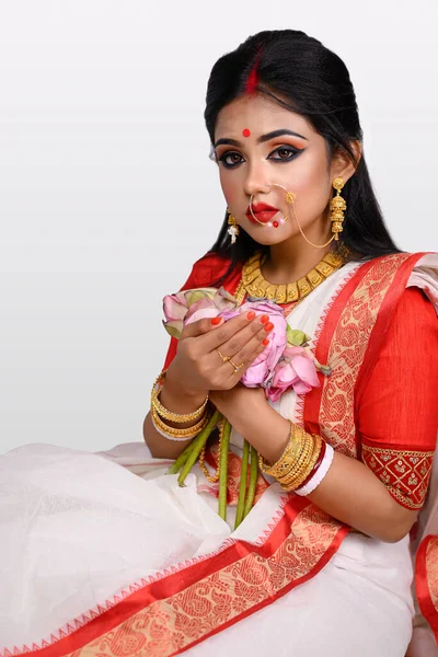 白い背景の前に座っている彼女の手に花を保持する伝統的なインドののこぎり 金のジュエリーやバングルを身に着けているかなり若いインドの少女の肖像画 インドの文化と伝統 — ストック写真