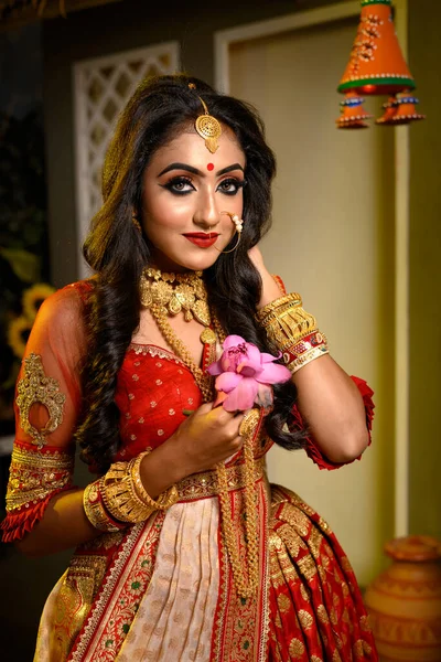照片上漂亮的年轻印度女孩戴着传统的萨里 手里拿着黄金珠宝和手镯 手握鲜花 在室内放光 印度文化 宗教和时尚 — 图库照片