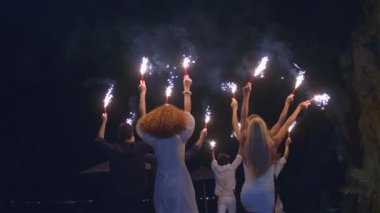 Gece eğlencesi. İnsanlar ellerinde konfeti ve havai fişeklerle koşuştururken eğleniyorlar. Farklı ırktan genç dostların yavaş çekimleri birlikte eğleniyor geceleri plajda maytap ve koşuşturuyorlar..