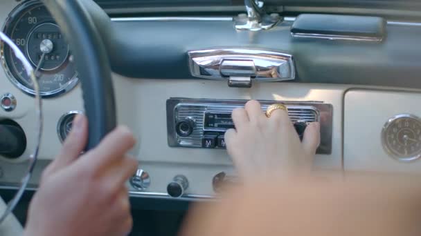 アンティークカーとラジオチャンネルがチューニングされています 老車の中で夫婦が旅をしている間に 女性はラジオをつけ チャンネルを探します レトロでビンテージカー クローズアップ撮影 — ストック動画