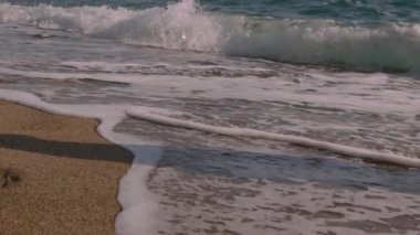 Kumların üzerinden deniz dalgaları geliyor. Sahilde, yakın plan, deniz dalgaları. Köpük ve köpük. Yüksek çerçeve oranı ve yavaş çekim.