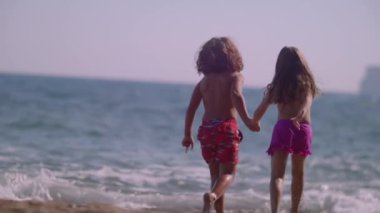 Deniz kenarında koşan çocuklar. Çocuklar denizde koşuyor, kıyılarında ve sahillerinde. Sahilden denize koşuyorlar. Yavaş çekim ve yüksek kalite