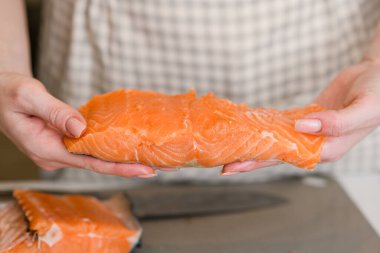 Beyaz kadın ellerinde çiğ kırmızı somon balığı filetosu, yaklaşın. Önlüklü kadın elinde bir parça kırmızı balık tutuyor..