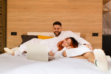 Bornozlu genç bir çift dizüstü bilgisayarla yatakta yatıyor. Kadın ve erkek film izliyor. Bir kadın başı bir erkeğin kucağında yatıyor..