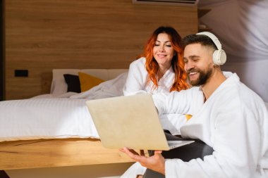 Yatakta dizüstü bilgisayarı olan bornozlu genç bir çift. Kadın ve erkek film izliyor. Yukarıdan görüntüle.