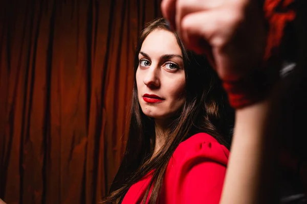 Bondage woman tied to bed with red ropes. Portrait of a young woman with tied hands to the headboard. Close-up.