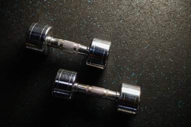 Spor salonunda iki parlayan metal dambıl yakın çekim halı, sağlıklı yaşam tarzı ve vücut geliştirme için spor malzemeleri. Yukarıdan görüntüle.
