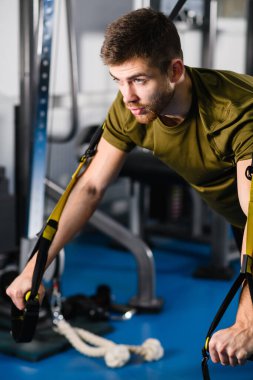 Spor salonunda beden eğitimi, sağlıklı yaşam tarzı, modern çapraz donanım ve spor egzersizleri için iç mekan eğitimi alan genç bir adam. Spor salonunda Trx egzersizi..