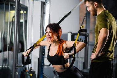 Spor koçu, modern spor ekipmanı, yan görüş, sağlıklı yaşam tarzı olan trx fitness kayışlarıyla şınav çeken sağlıklı bir kadın.