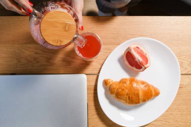 Kahvaltının en iyi manzarası fincana dökülen çay, greyfurt ve fırın kafenin ahşap masasında taze kruvasan, dışarıda dizüstü bilgisayarla çalışmak.