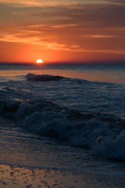 Deniz ve kızıl gökyüzü ile güzel bir gün batımı. Dikey fotoğraf, alçak çekim noktası. Önplanda deniz dalgaları.