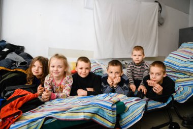 Dnipro, Ukrayna - 4 Nisan 2022: Bir grup kız ve erkek Dnipro 'daki bir mülteci merkezine dönüştürülmüş bir alışveriş merkezinde yataklarda oturuyor.