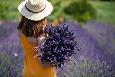 Sarı elbiseli bir kadın ve lavanta tarlasında kocaman bir demet lavanta çiçeği olan hasır şapkalı bir kadın..