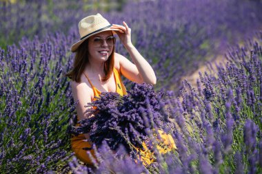 Hasır şapkalı genç bir kadın, lavanta tarlasında bir demet lavanta çiçeğiyle....