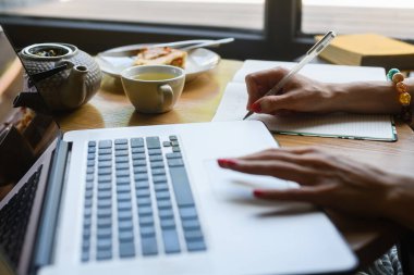 Close-up of a woman's hand working with a laptop in a coffee shop. A woman makes a note in her notebook while sitting in a cafe.
