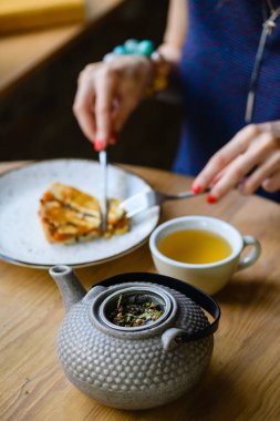 Kahve dükkanında bitki çayı ile çaydanlığın yakın çekimi. Kız kek yiyor ve çay içiyor..