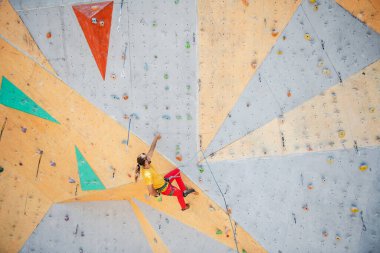 Genç ve formda bir adam dışarıda dağ tırmanışı yapıyor. Duvara tırmanan adam.