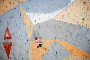 Sporcu kadın tırmanışçı dik kayalara tırmanıyor, yapay duvara tırmanıyor. Ekstrem spor ve kaya konsepti
